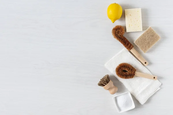 Eco friendly bamboo dish brushes and lemon with baking soda for cleaning top view on white wooden background. Zero waste concept. Plastic and chemistry free.