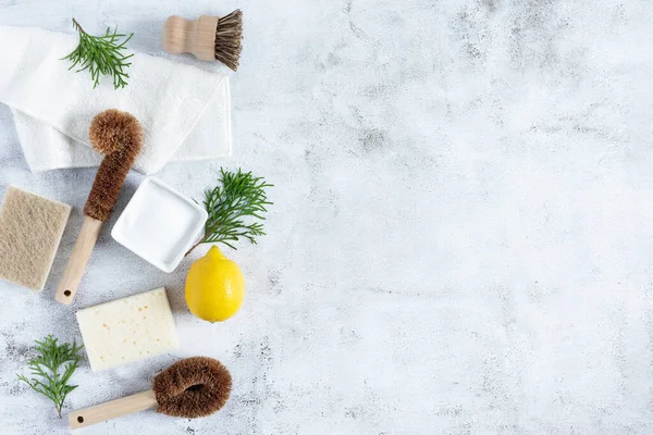 Eco friendly bamboo dish brushes and lemon with baking soda for cleaning top view on grey concrete background. Zero waste concept. Plastic and chemistry free.