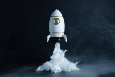 Siyah arka planda duman bulutu olan dekoratif roket oyuncağı, gerçekçi fırlatma efekti, eğitim, illüstrasyon ve yaratıcı uzay teması için ideal.