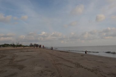 Sakin okyanusun üzerinde gün batımı suyun üzerine sıcak bir parıltı saçıyor. Gökyüzünün altındaki kumlu plaj turuncu ve pembe renkler mavi denize karışıyor.. 