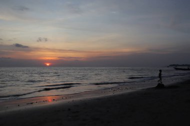 Sakin okyanusun üzerinde gün batımı suyun üzerine sıcak bir parıltı saçıyor. Gökyüzünün altındaki kumlu plaj turuncu ve pembe renkler mavi denize karışıyor.. 