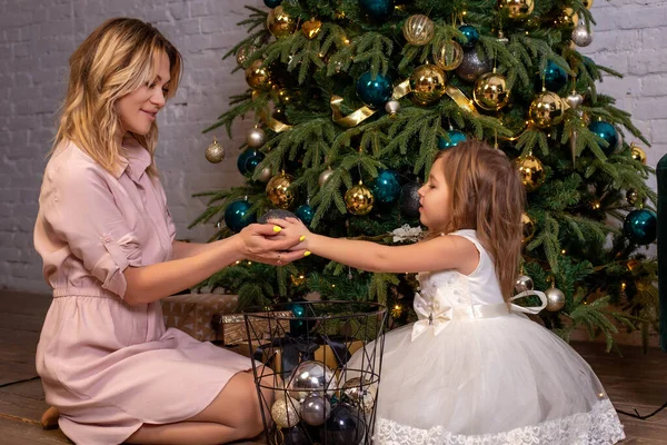 Merry Christmas and Happy Holidays. The family decorates the holiday tree. Mother and daughter decorate the Christmas tree. Happy mother giving a Christmas present. New Year