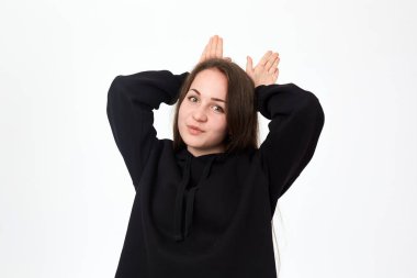 Beyaz arka plan üzerinde dururken bir tavşan kulakları gibi avuç içi tutan siyah bir sweatshirt güzel bir genç esmer kadın Stüdyo çekim.