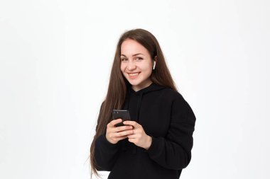 Beyaz arka plan üzerinde dururken kablosuz kulaklık ve telefon ile kamera mutlu görünümlü güzel bir genç esmer kadın Stüdyo çekim.