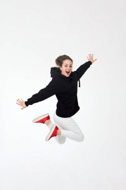 Siyah kapüşonlu, beyaz pantolonlu ve kırmızı spor ayakkabılı genç, güzel esmer kız beyaz arka planda tek başına zıplıyor..