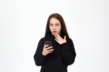 Cep telefonu tutan kablosuz kulaklık ve beyaz arka plan üzerinde dururken kameraya bakarak güzel bir genç esmer kadın Stüdyo çekim.