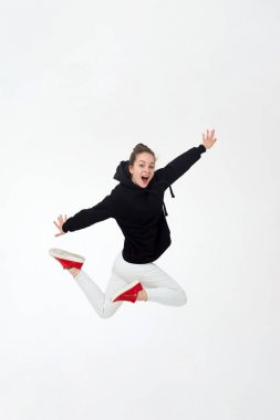 Siyah kapüşonlu, beyaz pantolonlu ve kırmızı spor ayakkabılı genç, güzel esmer kız beyaz arka planda tek başına zıplıyor..