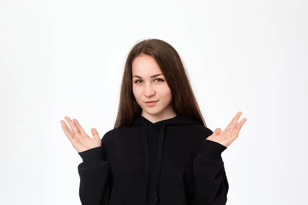 Foto de estudio de una hermosa mujer joven con una sudadera negra expresando emoción de duda mientras está de pie sobre fondo blanco y encogiéndose de hombros . — Foto de Stock