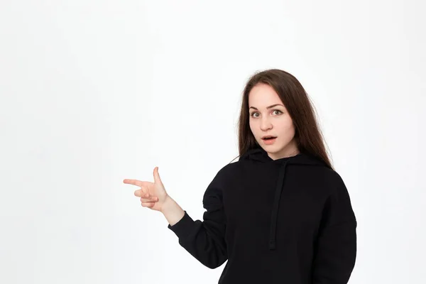 Portrait d'une jolie jeune brune en sweat noir sur fond blanc pointant les doigts vers la gauche . — Photo