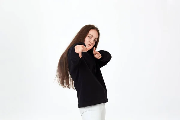 Retrato de una hermosa mujer joven positiva con una sudadera negra y pantalones blancos sobre un fondo blanco apuntando a la cámara con las manos — Foto de Stock