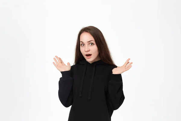 Foto de estudio de una hermosa joven con una sudadera negra expresando emoción de sorpresa mientras estaba de pie sobre un fondo blanco y encogiéndose de hombros . —  Fotos de Stock