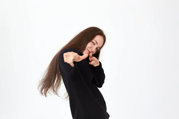 Siyah sweatshirt ve beyaz bir arka plan üzerinde beyaz pantolon ile olumlu bir güzel genç kadın portresi elleri ile kamera işaret — Stok fotoğraf