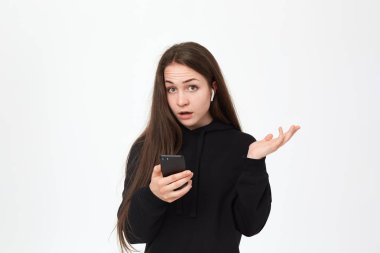 Cep telefonu tutan kablosuz kulaklık ve beyaz arka plan üzerinde dururken kameraya bakarak güzel bir genç esmer kadın Stüdyo çekim.