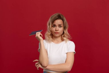 Portrait of a beautiful girl with curly blond hair dressed in a white t-shirt standing on a red background.  clipart