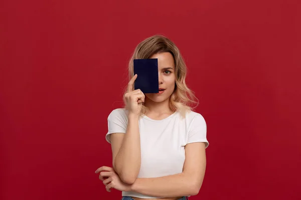 Kırmızı bir arka plan üzerinde duran beyaz bir t-shirt kıvırcık sarı saçlı bir kızın portresi. Model kameraya gülümsüyor ve bir yüzün yarısını kaplayan mavi renk pasaport tutar.