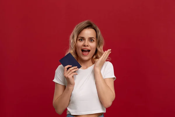 Porträt eines schönen Mädchens mit lockigem blondem Haar, bekleidet mit einem weißen T-Shirt, das auf rotem Hintergrund steht. — Stockfoto