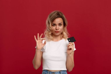 Kırmızı bir arka plan üzerinde duran beyaz bir t-shirt kıvırcık sarı saçlı bir kızın portresi. Model kameraya gülümsüyor, bir yüzün yarısını kaplayan banka kartı tutar ve Ok-sembolü jest gösteren.