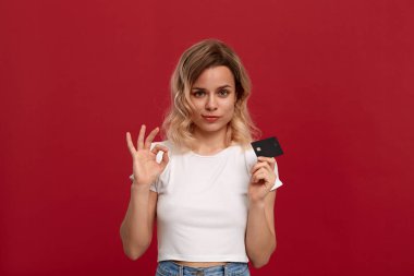Kırmızı bir arka plan üzerinde duran beyaz bir t-shirt kıvırcık sarı saçlı bir kızın portresi. Model kameraya gülümsüyor, bir yüzün yarısını kaplayan banka kartı tutar ve Ok-sembolü jest gösteren.