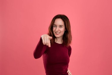 Size işaret ederken siyah pembe arka plan üzerinde izole ayakta mutlu genç bayan kamera bakıyor