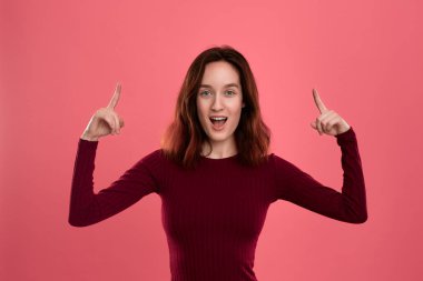 Heyecanlı genç bayan ayakta koyu pembe arka plan üzerinde parmaklarla işaret üzerinde izole. Reklam için yer