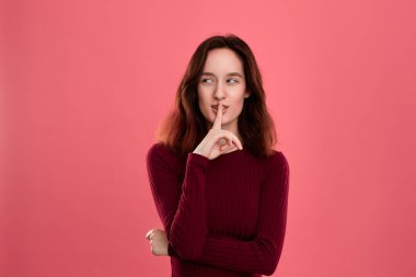 Parmak ile koyu pembe arka plan üzerinde izole güzel genç bayan ayakta sessizlik tutmak ve kameraya bakarak jest ifade yakın kaldırdı.