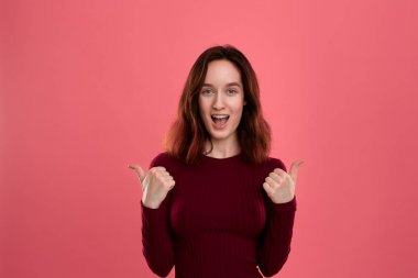 Mutlu genç bayan ayakta pozitif değerlendirme vererek başparmak ile koyu pembe arka plan üzerinde izole.
