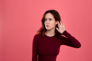 Bazı söylentiler dinlerken gibi elleri kulak yakın yükseltilmiş ile koyu pembe arka plan üzerinde izole ayakta sürpriz genç bayan.