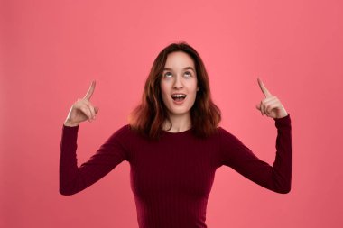 Heyecanlı genç bayan ayakta koyu pembe arka plan üzerinde parmaklarla işaret üzerinde izole. Reklam için yer