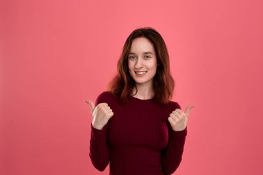 Mutlu genç bayan ayakta pozitif değerlendirme vererek başparmak ile koyu pembe arka plan üzerinde izole.