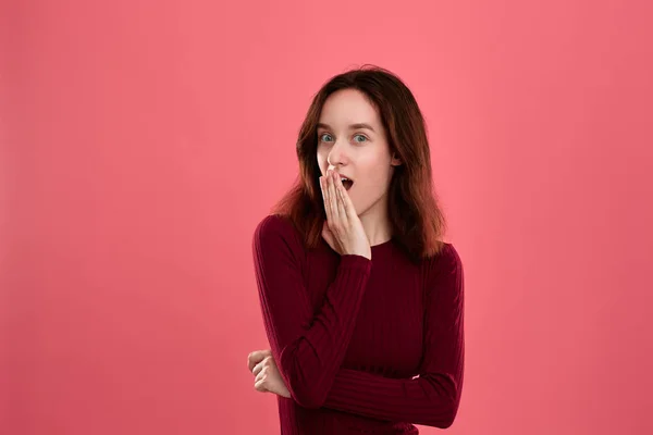 Überraschte junge Frau, die isoliert vor dunkelrosa Hintergrund steht und die Hände in der Nähe des Mundes erhebt, um Emotionen des Schocks auszudrücken. — Stockfoto