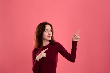 Koyu pembe arka planda bir parmak ile sağ üst köşesinde işaret izole ayakta mutlu genç bayan. Reklam için yer