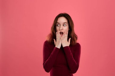 Şaşırtıcı genç bayan ayakta koyu pembe arka plan üzerinde elleri ile yakın ağız şok duygu ifade yükseltilmiş.