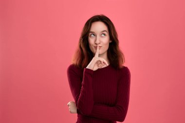 Parmak ile koyu pembe arka plan üzerinde izole güzel genç bayan ayakta sessizlik tutmak ve kameraya bakarak jest ifade yakın kaldırdı.