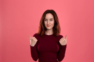 Mutlu genç bayan ayakta pozitif değerlendirme vererek başparmak ile koyu pembe arka plan üzerinde izole.