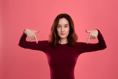 Heyecanlı genç bayan ayakta koyu pembe arka planda parmaklarla aşağı işaret üzerinde izole. Reklam için yer