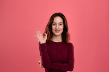Koyu pembe arka plan üzerinde izole duran mutlu genç bayan Ok işareti jest gösteren gözünün yanında bir el avuç tutarken kameraya bakar.