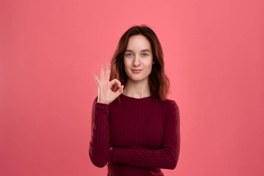 Koyu pembe arka plan üzerinde izole duran mutlu genç bayan Ok işareti jest gösteren gözünün yanında bir el avuç tutarken kameraya bakar.