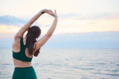 Genç esmer kadın müzik dinlerken gün doğumunda deniz kıyısında egzersiz.