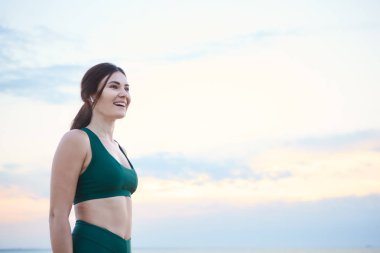 Genç esmer kadın müzik dinlerken gün doğumunda deniz kıyısında egzersiz.