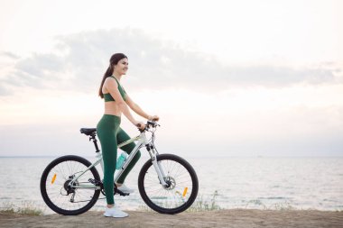 Gün doğumunda bisiklete binen genç esmer kadın.