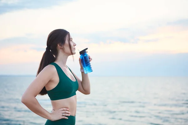Fiatal barna nő vezeték nélküli fülhallgatók és okos órák pihenő után reggel edzés ivóvíz. — Stock Fotó