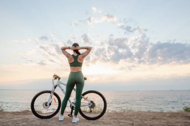 Güzel genç esmer kadın güneşin doğuşunda bisiklet yolculuğu sonra istirahat. Sabah kablosuz kulaklıklarla müzik dinleme modeli.