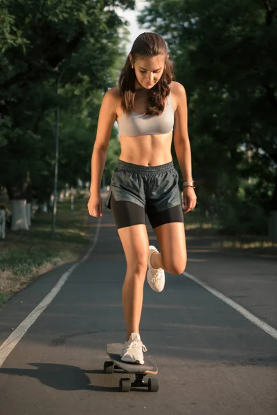 Porträtt av en ung brunett kvinna skateboard på en väg i parken. — Stockfoto