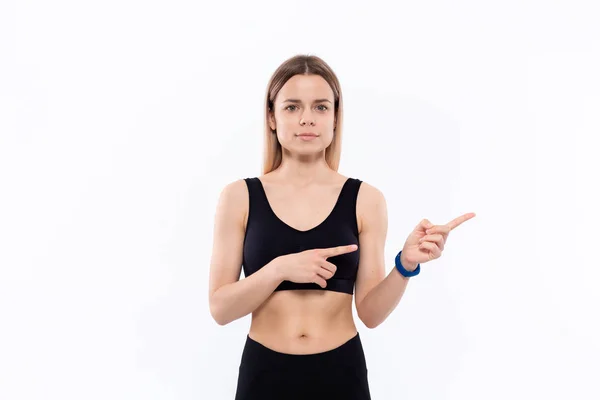 Ung sportig blond kvinna i svart sportkläder med smarta klockor för pulsmätning som pekar med fingrarna åt höger. — Stockfoto