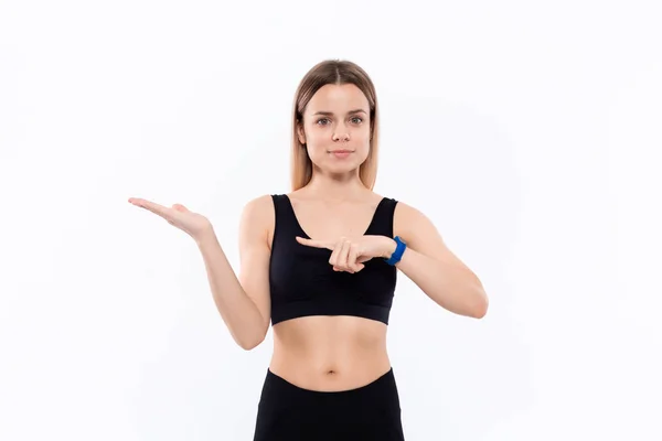 Ung sportig blond kvinna i en svart sportkläder med smarta klockor för pulsmätning pekar med en hand på löper av en hand — Stockfoto