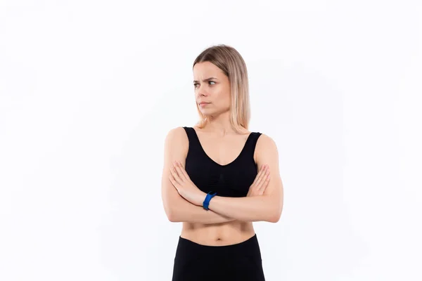 Joven mujer rubia deportiva en una ropa deportiva negra con relojes inteligentes para medir el pulso manteniendo las manos cruzadas de pie sobre fondo blanco . — Foto de Stock