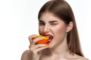 Parlak renk makyaj ile güzel bir genç kadının seyir portre yüz yakın bir portakal yarım ısırma.