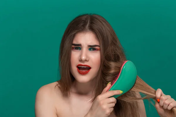 Portrait of beautiful young woman with bright color make-up combing hair with a green brush