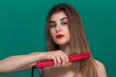 Parlak renk makyaj ile güzel genç kadının portresi mor bir düzleştirme demir ile saç tarzı kendini yapıyor.