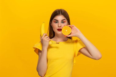 Sarı tee genç model sarı arka plan üzerinde muz ve turuncu ayakta tutar.